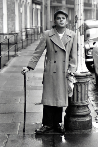 Singer Ian Dury in street with walking stick, 1970s